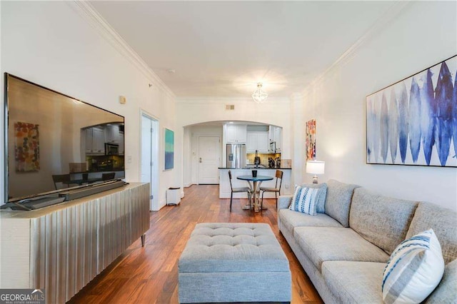 living area with dark wood-style floors, crown molding, and arched walkways