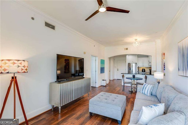 living room featuring dark wood-style flooring, visible vents, crown molding, a ceiling fan, and arched walkways