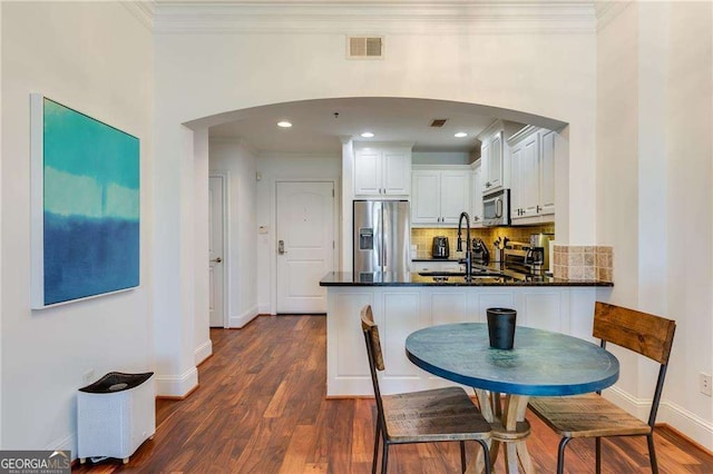 dining area with visible vents, baseboards, ornamental molding, dark wood finished floors, and arched walkways