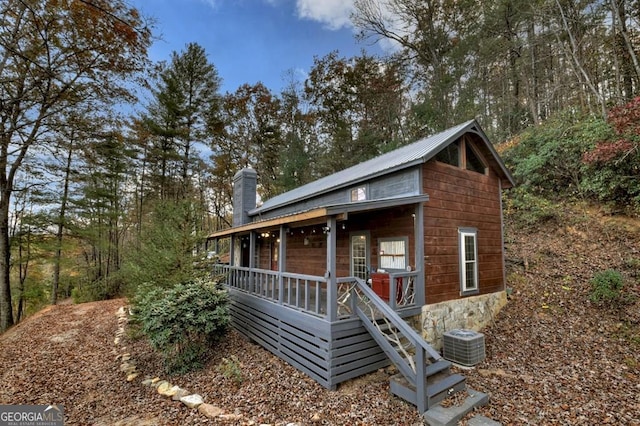 chalet / cabin featuring covered porch, a chimney, and central AC