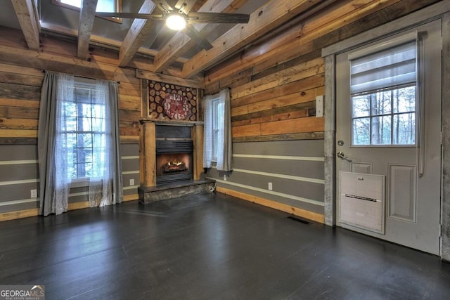 unfurnished living room featuring visible vents, wooden walls, a ceiling fan, beam ceiling, and a stone fireplace