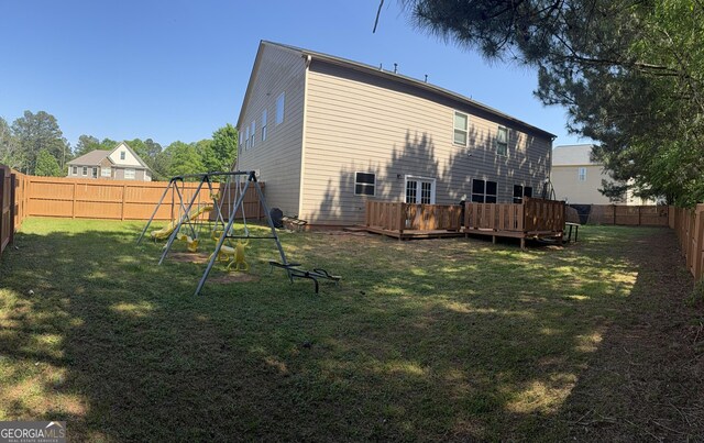 back of property featuring a fenced backyard, a wooden deck, a playground, and a lawn