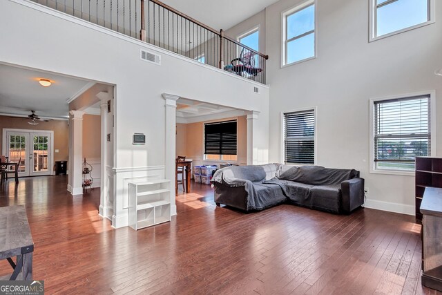 living room featuring wood-type flooring, ornate columns, visible vents, a towering ceiling, and ceiling fan