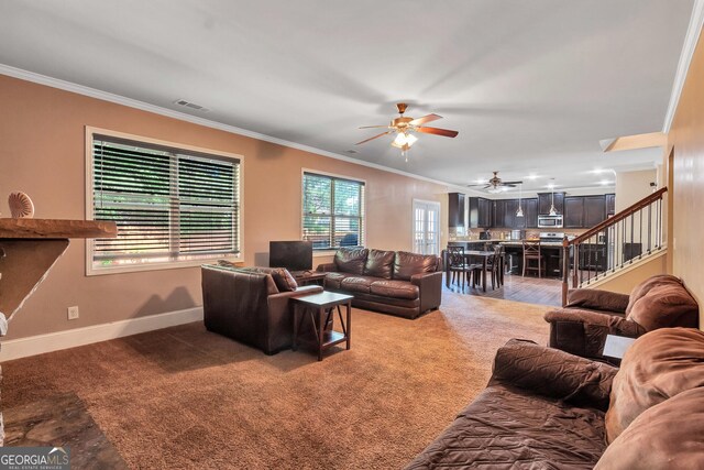 carpeted living area with baseboards, ornamental molding, ceiling fan, visible vents, and stairs