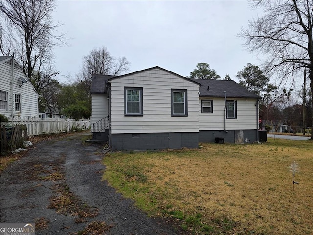 rear view of house with aphalt driveway, a shingled roof, fence, and a yard