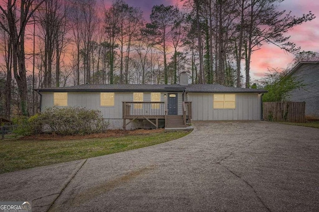 view of front facade with board and batten siding, a chimney, concrete driveway, and fence