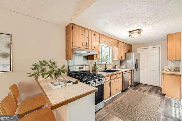 kitchen with a sink, tasteful backsplash, appliances with stainless steel finishes, under cabinet range hood, and tile countertops