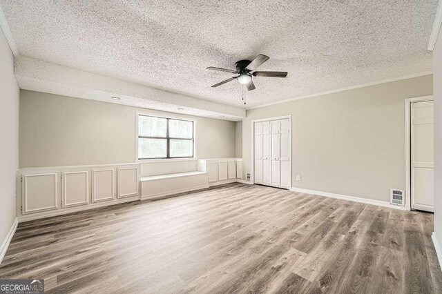 unfurnished room featuring crown molding, wood finished floors, a textured ceiling, baseboards, and ceiling fan