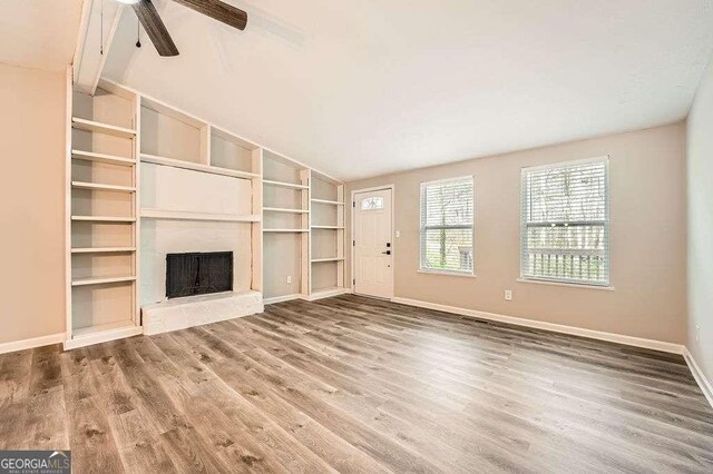 living area with light wood-type flooring, ceiling fan with notable chandelier, a fireplace with raised hearth, baseboards, and vaulted ceiling with beams