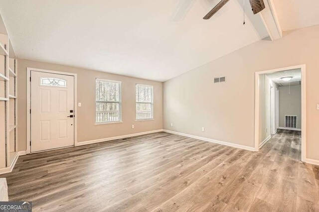 unfurnished living room with vaulted ceiling, a fireplace with raised hearth, baseboards, a ceiling fan, and wood finished floors