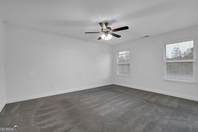 spare room with visible vents, baseboards, a ceiling fan, and dark colored carpet