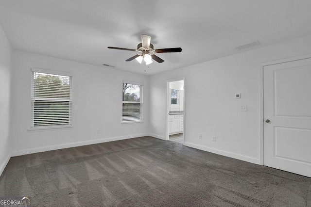 spare room featuring dark colored carpet, visible vents, baseboards, and ceiling fan