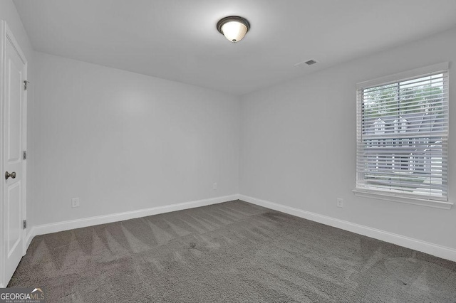 spare room featuring dark carpet, baseboards, and visible vents
