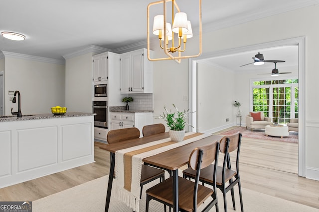 dining area with ornamental molding, ceiling fan with notable chandelier, and light wood finished floors