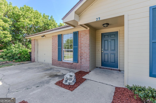entrance to property featuring an attached garage, brick siding, and driveway