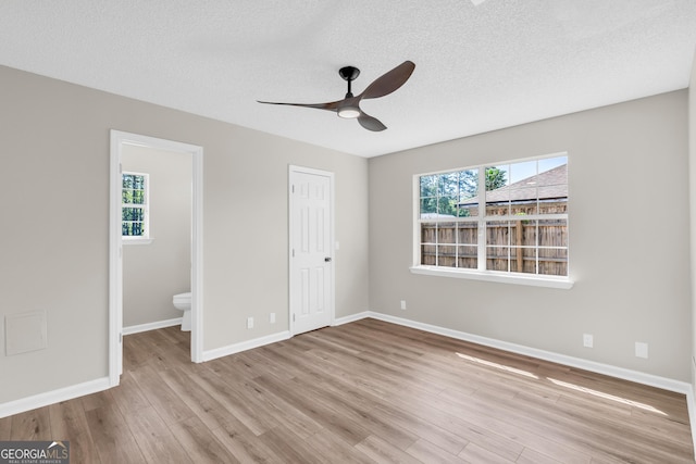unfurnished bedroom with baseboards, wood finished floors, a textured ceiling, and connected bathroom
