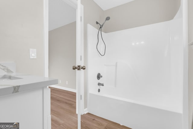 full bathroom featuring washtub / shower combination, wood finished floors, vanity, and baseboards