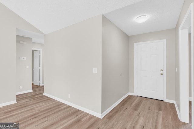 foyer featuring baseboards, lofted ceiling, and light wood finished floors