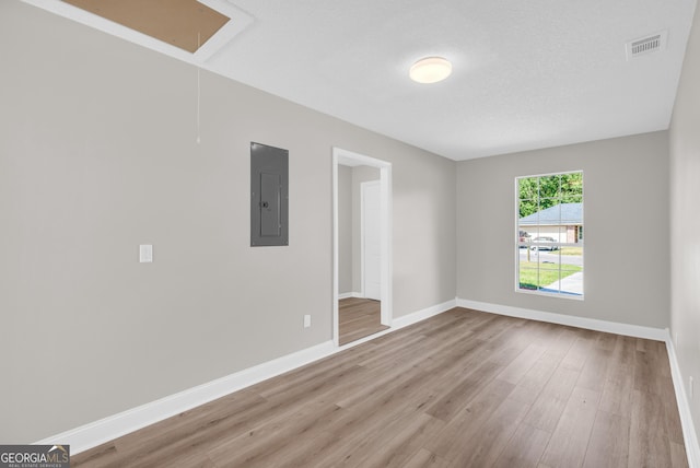 empty room featuring wood finished floors, visible vents, electric panel, baseboards, and attic access