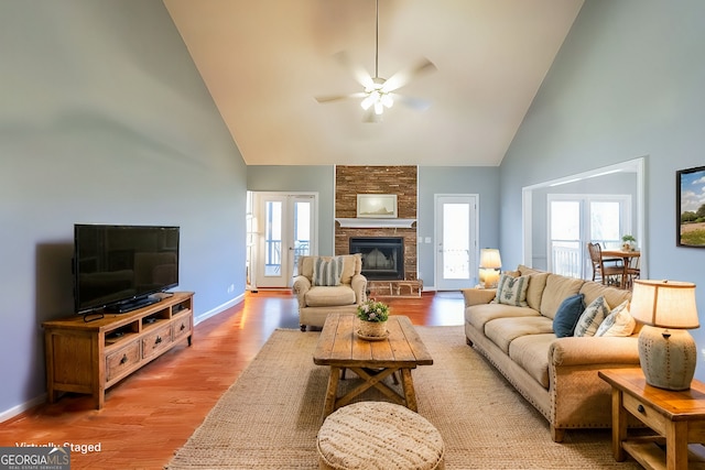 living room featuring high vaulted ceiling, a ceiling fan, light wood-type flooring, baseboards, and a fireplace