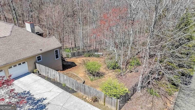 view of home's exterior with roof with shingles, fence, stucco siding, driveway, and a chimney