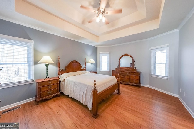 bedroom featuring a raised ceiling, light wood-style floors, baseboards, ceiling fan, and ornamental molding