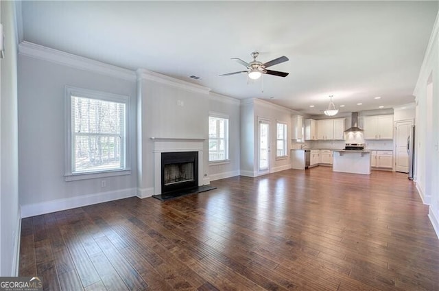 unfurnished living room with dark wood-style flooring, crown molding, baseboards, and a ceiling fan