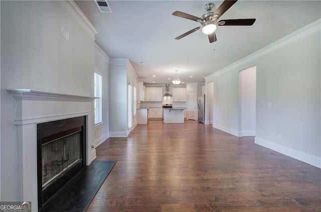 unfurnished living room featuring dark wood-style flooring, visible vents, a fireplace with raised hearth, ceiling fan, and crown molding
