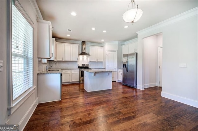 kitchen featuring wall chimney range hood, a center island, stainless steel appliances, white cabinetry, and ornamental molding