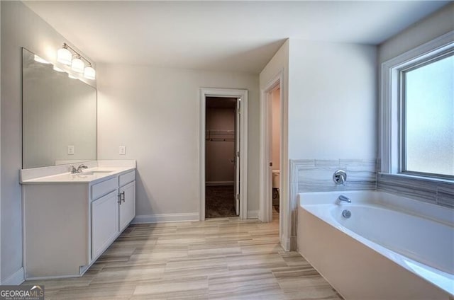 bathroom with baseboards, a garden tub, vanity, and a spacious closet