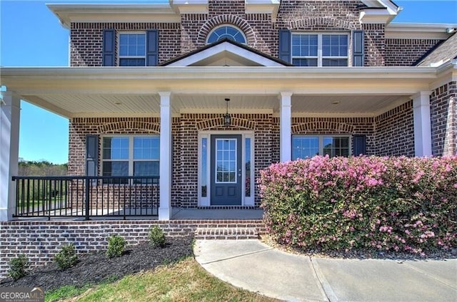 view of exterior entry featuring brick siding and a porch