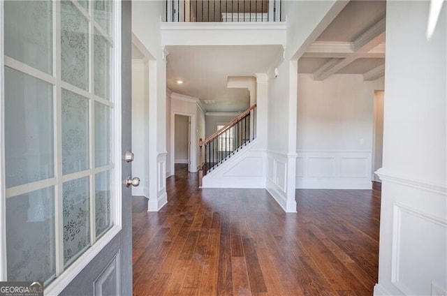 entrance foyer featuring dark wood-style flooring, beamed ceiling, stairs, a decorative wall, and ornamental molding