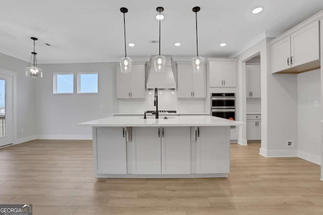 kitchen featuring light countertops, light wood finished floors, double oven, custom range hood, and backsplash