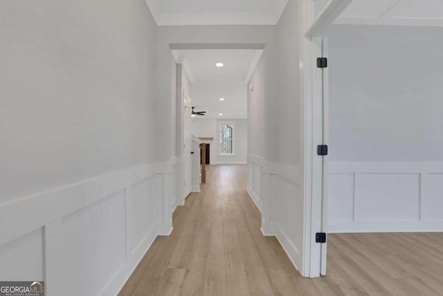 corridor featuring wainscoting, a decorative wall, ornamental molding, and light wood finished floors