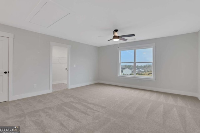 carpeted empty room with a ceiling fan, baseboards, and attic access