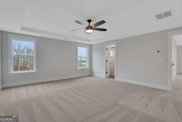 carpeted spare room featuring a tray ceiling, baseboards, ceiling fan, and visible vents