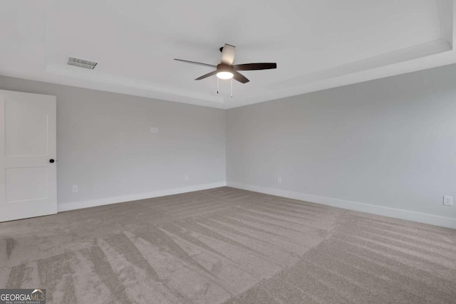 carpeted empty room featuring a tray ceiling, baseboards, visible vents, and a ceiling fan
