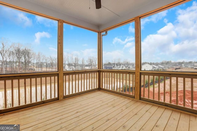 unfurnished sunroom with a residential view, a wooden deck, ceiling fan, and wood-type flooring