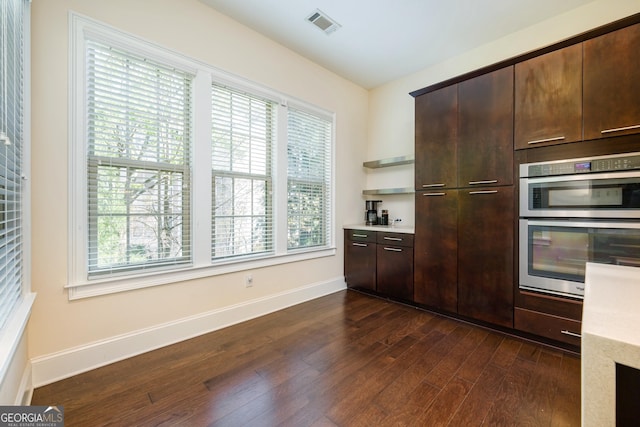 kitchen with stainless steel double oven, dark wood-type flooring, baseboards, visible vents, and dark brown cabinetry
