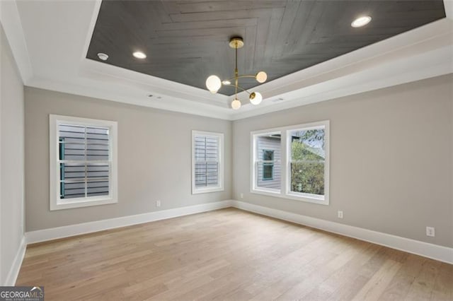 unfurnished room with an inviting chandelier, baseboards, light wood-type flooring, a tray ceiling, and ornamental molding
