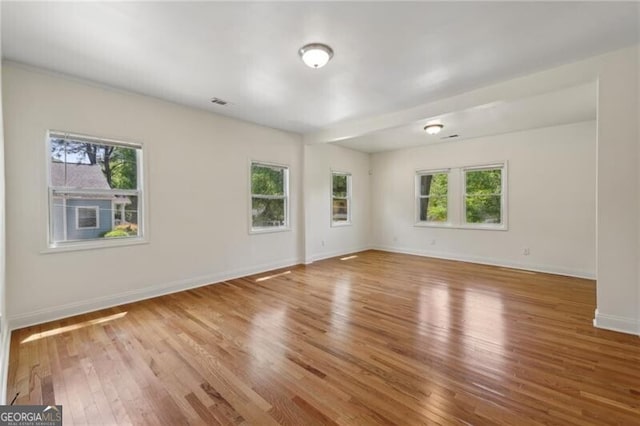 unfurnished room with a wealth of natural light, wood finished floors, and baseboards