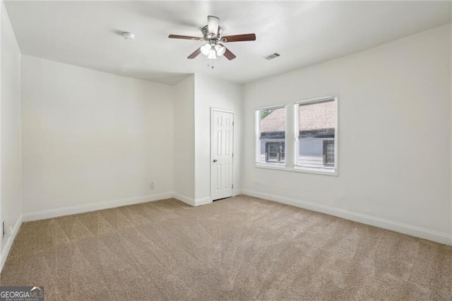 carpeted spare room with visible vents, a ceiling fan, and baseboards