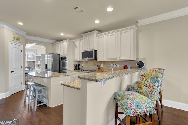 kitchen with a breakfast bar area, stainless steel appliances, decorative backsplash, a kitchen island, and arched walkways