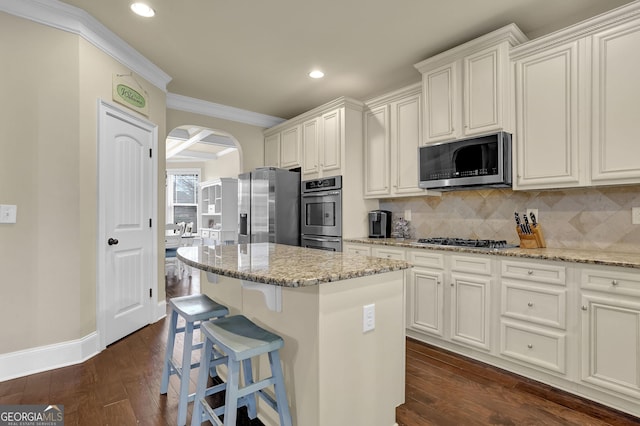kitchen with crown molding, a center island, stainless steel appliances, arched walkways, and dark wood-style flooring