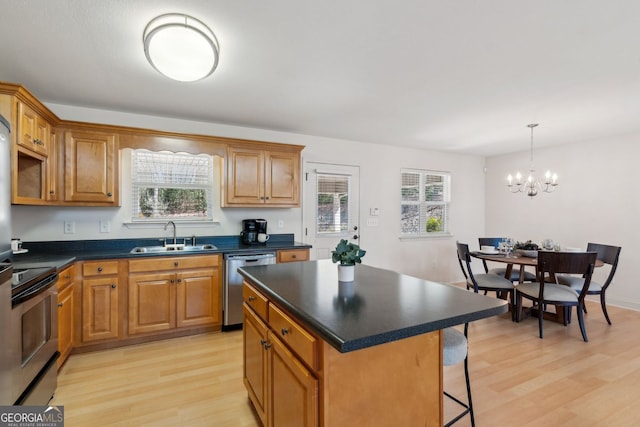 kitchen with a sink, a breakfast bar area, appliances with stainless steel finishes, dark countertops, and an inviting chandelier