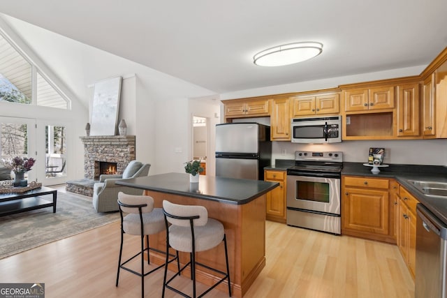 kitchen featuring light wood finished floors, a kitchen breakfast bar, a center island, stainless steel appliances, and dark countertops