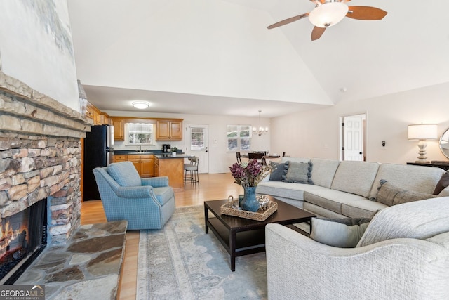 living room featuring high vaulted ceiling, light wood-style flooring, and ceiling fan with notable chandelier