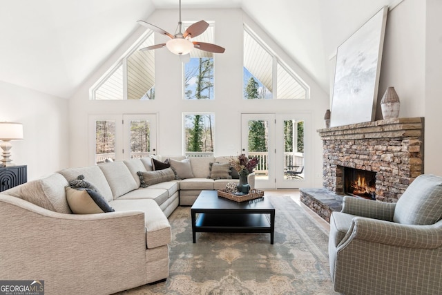living area featuring ceiling fan, vaulted ceiling, and a stone fireplace