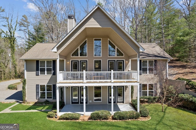 view of front facade with a front lawn, a chimney, a shingled roof, and a patio