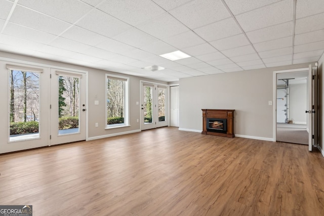 unfurnished living room featuring baseboards, a glass covered fireplace, a paneled ceiling, and light wood finished floors